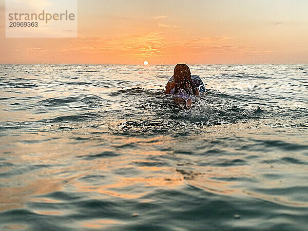 From behind young girl paddle board in Gulf of Mexico sunset