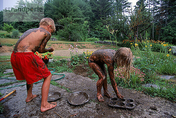 A young brother and sister play in the mud in Maine.