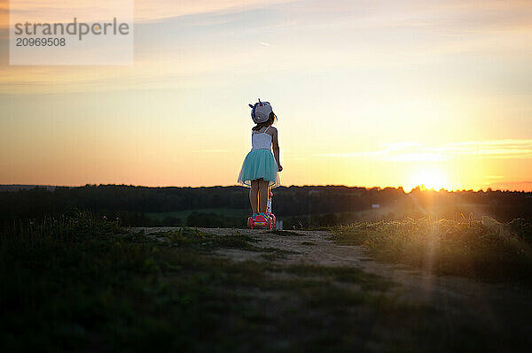 From behind young girl on scooter at sunset