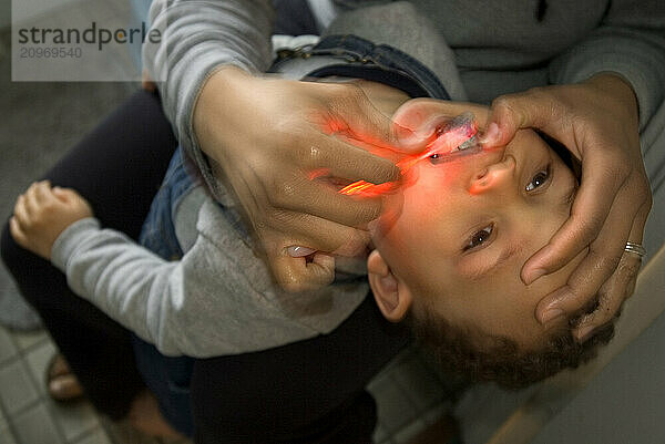 A boy is getting his teeth brushed by his mother