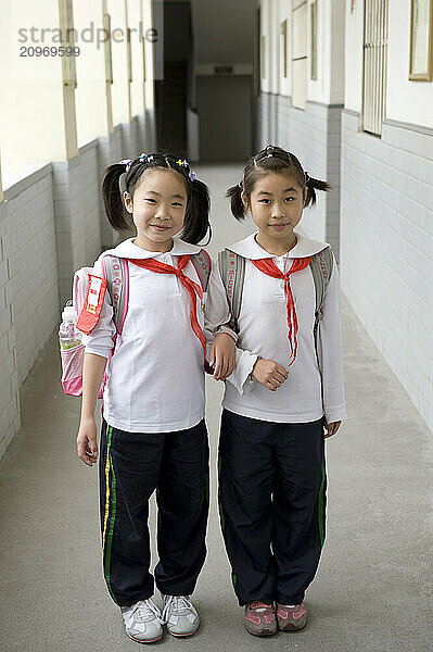 Two young girls walking down a school hallway to their next class.