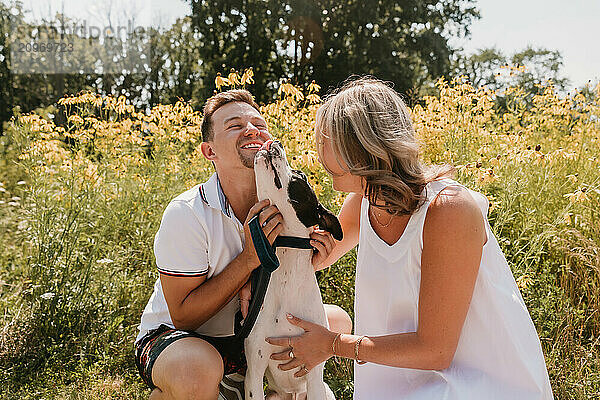 Smiling young couple with their dog in front of wildflowers