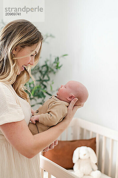 Mom smiles down at newborn baby with white background.