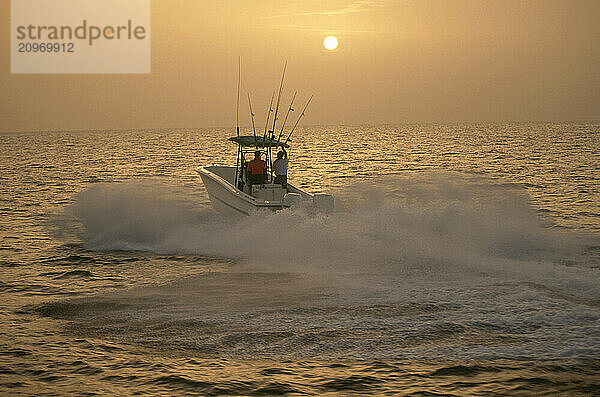 Two guys heading out in their boat to sea to fish as the sun sets in the distance.