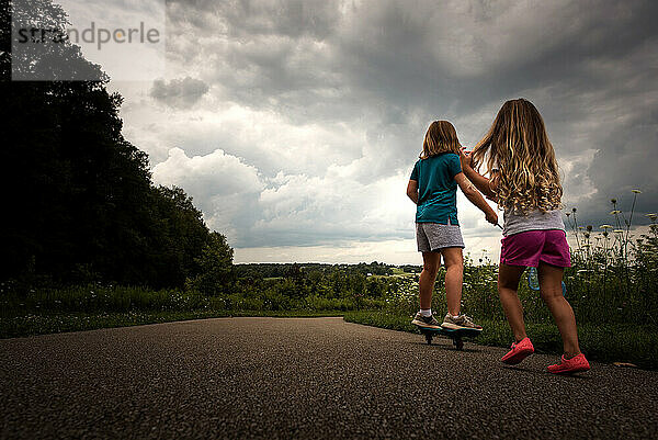 Young sisters riding skateboard outdoors dramatic sky