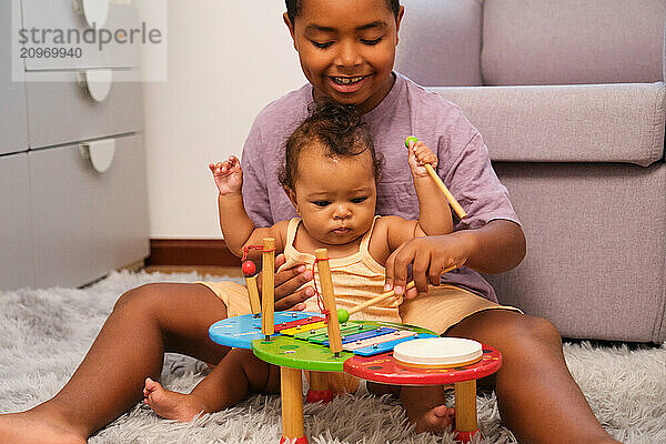 Brother teaching baby sister how to play music on xylophone