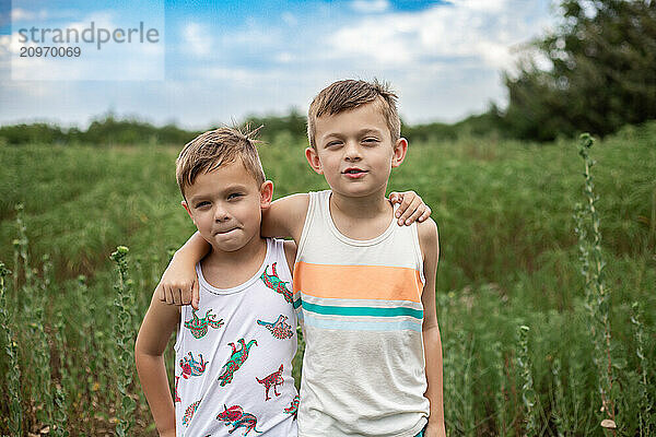 portrait of two boys smiling in field under blue sky