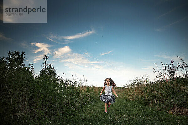 Beautiful young girl running down green path blue sky