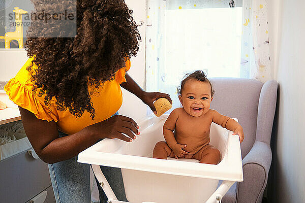 Mother is giving a bath to her baby girl in a bathtub