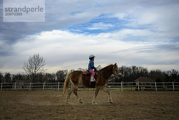 Young girl in helmet riding brown pony in pature