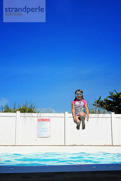 Young girl jumping into swimming pool wearing goggles