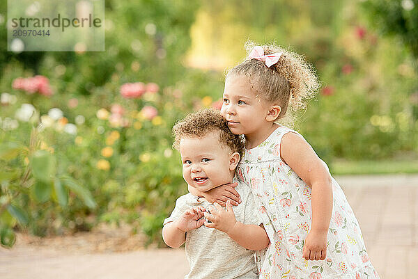 Sister hugging brother in garden of flowers