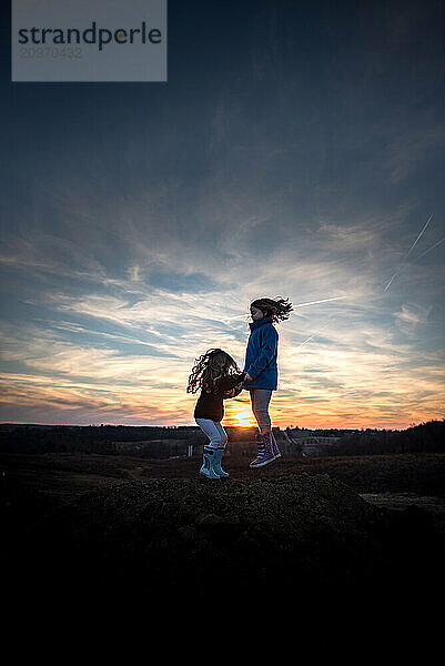 Young sisters jumping and playing on dirt pile at sunset