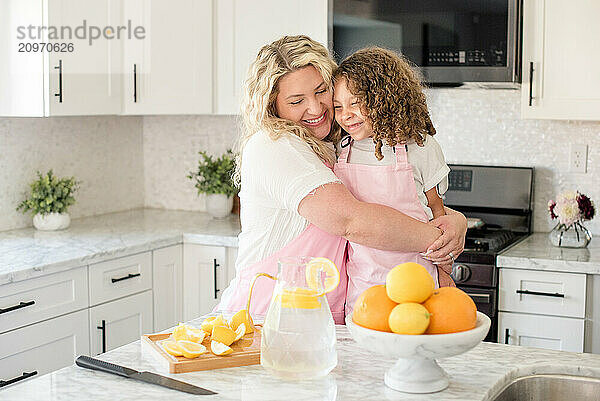 Mother hugging little daughter in the kitchen with lemonade