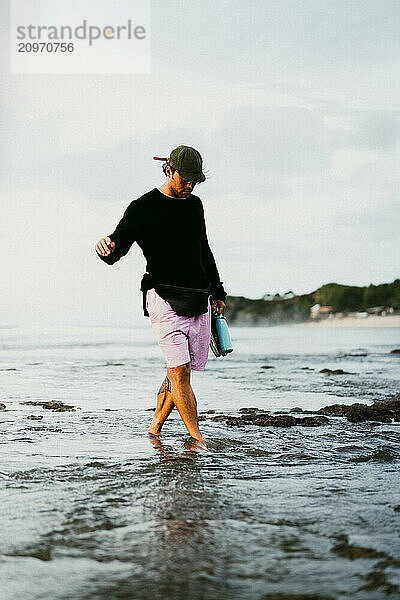 A young man walks along the caral reef on the beach in Bali.