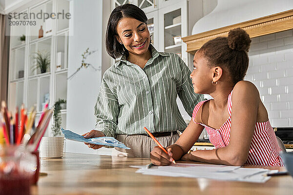 Afro woman and kid girl doing homework drawing on breakfast together