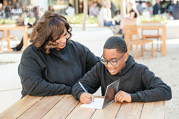 Child writing in his notebook with aunt helping