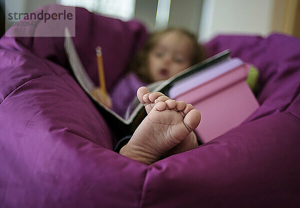 Close up of little girl's toes laying in bean bag doing homework