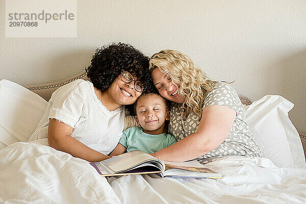 Mother and daughters cuddle in bed with book on lap