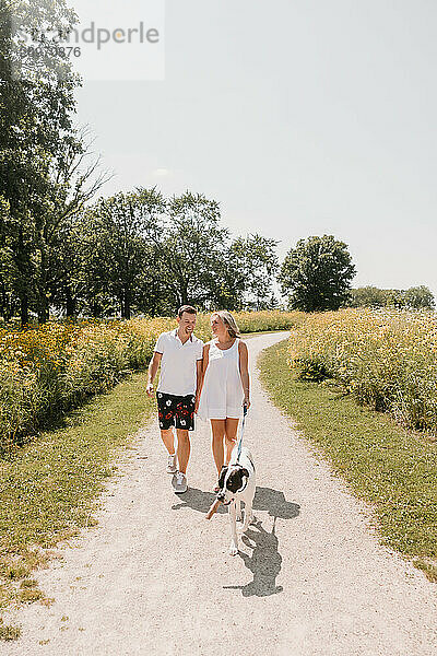 Young couple walking with dog on path lined with wildflowers.