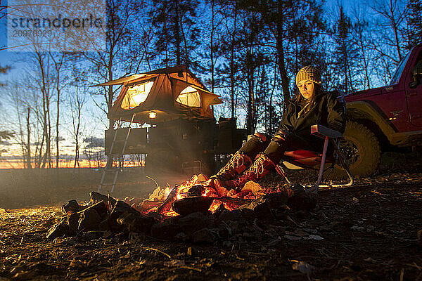 Young woman sitting by campfire in forest  Biwabik  Minnesota  USA