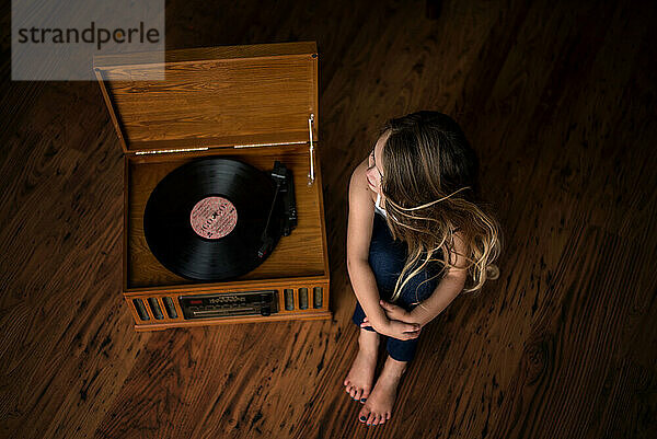 Beautiful young girl listening to vinyl on record player indoors