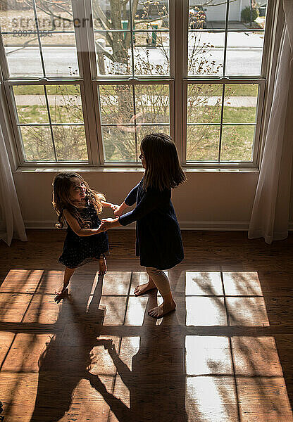 Happy young sisters dancing indoors on dark wooden floor