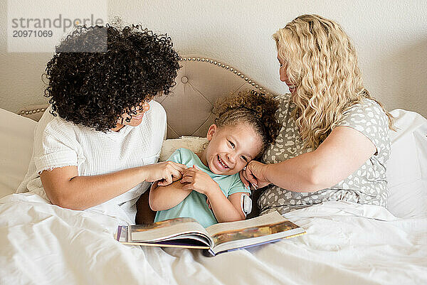 Little girl being tickled by mother and big sister in bed