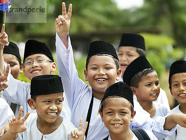 A group of young Muslim boys waving hello and holding their hands up in the 'Peace' sign to the camera.