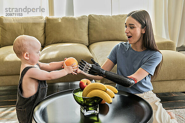 Young woman with prosthesis puts fruits with baby boy