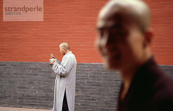 Monks eat lunch in front of a red wall at The Shaolin Temple in China.