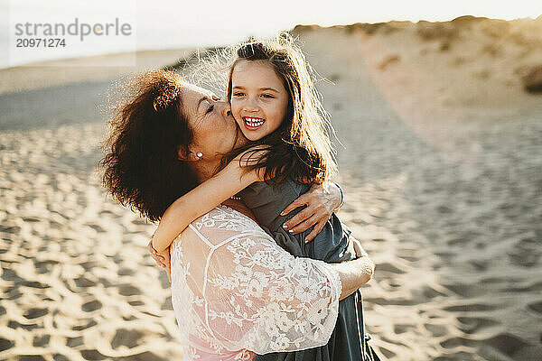 Grandma hugging kissing beautiful grandchild girl at beach