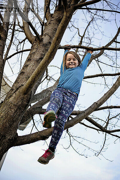 Young girl hanging from tree branch from above