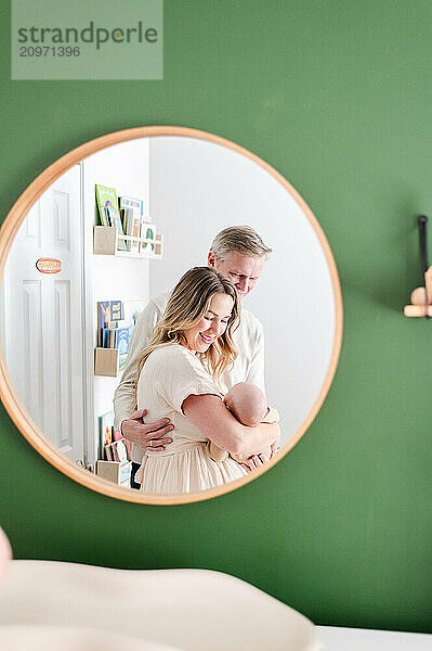 Reflection in round mirror of parents smiling at newborn baby.