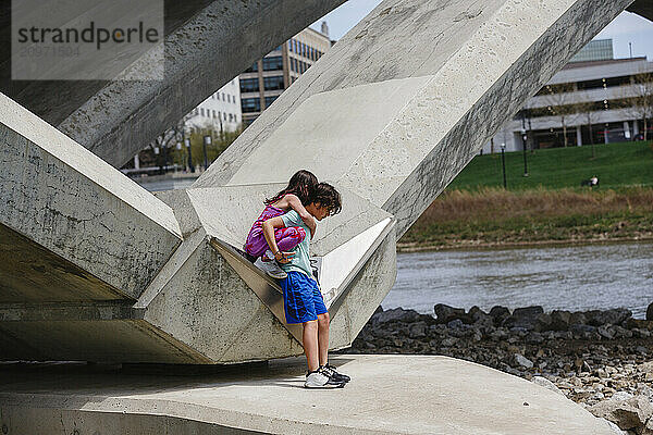 Little boy carries small girl off bridge piling