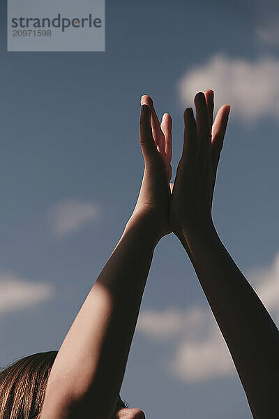 Kid's hands raised up against the blue sky