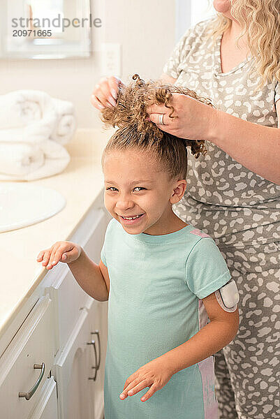 Little girl getting her hair put up in a pony tail by her mother