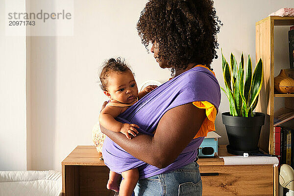 Mother holding her baby in a purple wrap at home