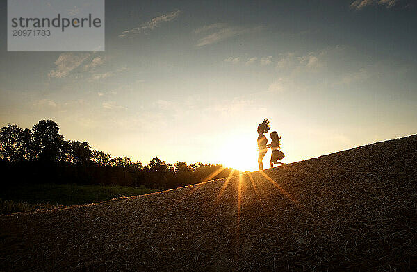 Young sisters running down hill through sunburst