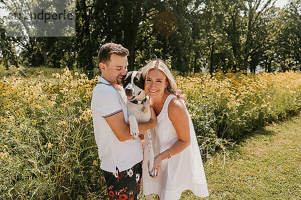 Smiling young couple with their dog in front of wildflowers