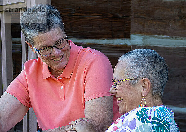 Older gay couple smiling and chatting on porch steps