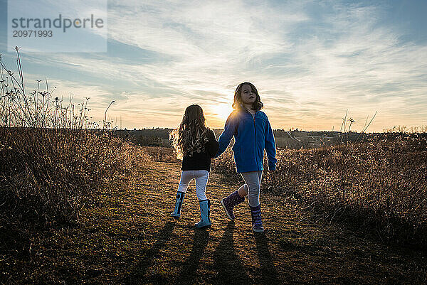 Young sisters walking down sunny path at sunset