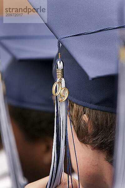 Close up  rear view of male students in graduation caps and gowns  awaiting their diplomas at their high school graduation.