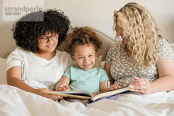 Mother with two daughters in bed reading a book