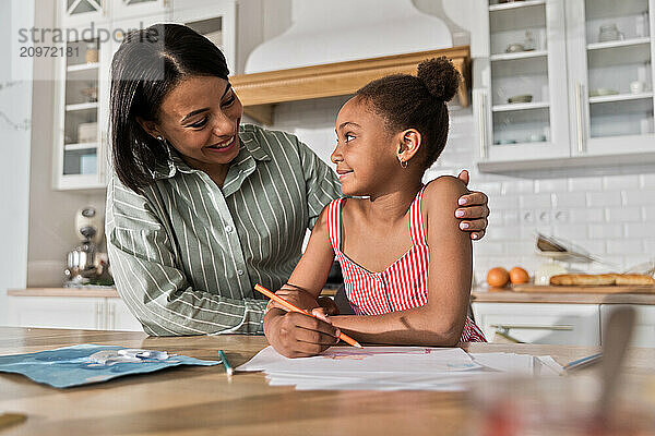 Afro woman and kid girl doing homework drawing on breakfast together