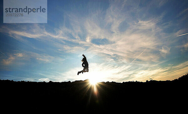 Young girl jumping over sunburst against blue sky