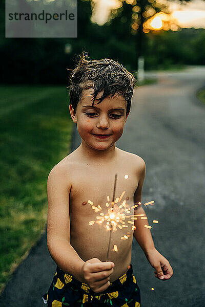 Boy holding a lit sparkler  smiling  evening setting