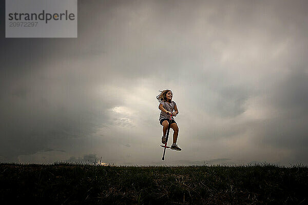 Young girl on pogo stick dramatic sky