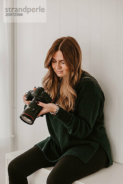 Smiling woman holding a camera  sitting in a bright room