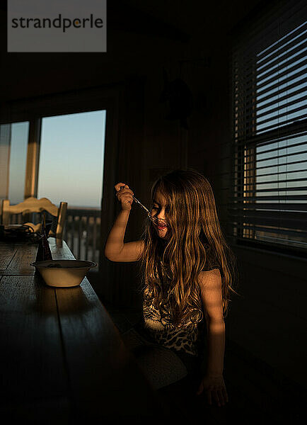 Young girl eating at table indoors in warm sunlight